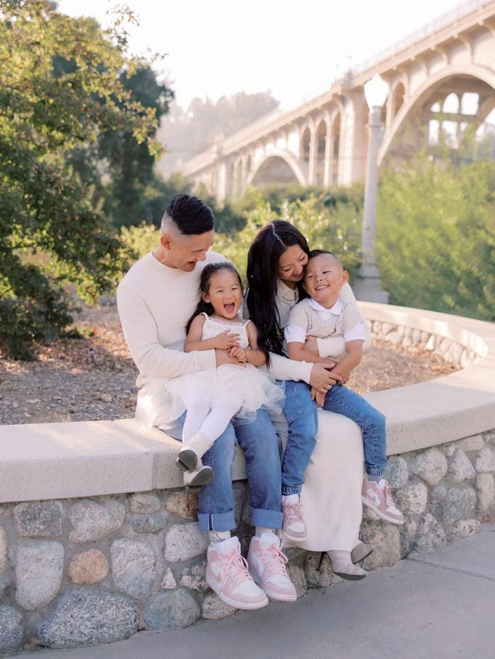 Parents and kids laughing on a stone wall below a Pasadena bridge